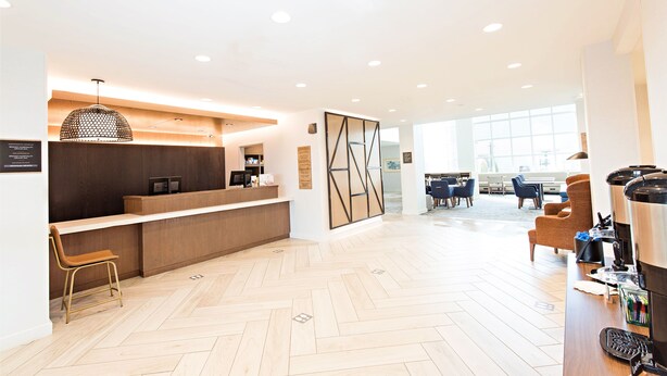 A modern reception area with a wooden counter, a seating area with chairs, and a coffee station. - Staybridge Suites Denver North - Thornton by IHG (Thornton)