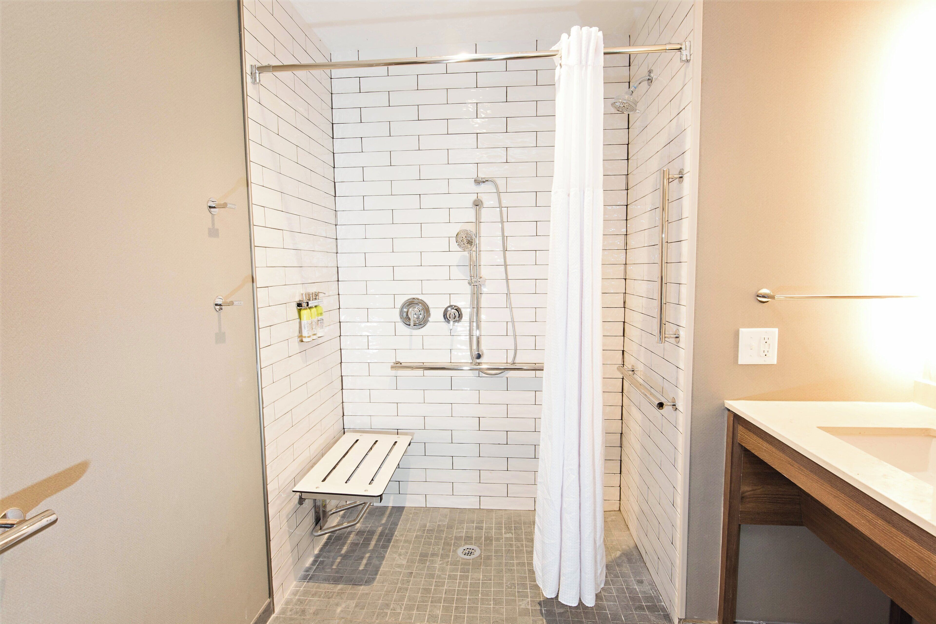 Une douche avec un rideau blanc, un banc et un mur carrelé.