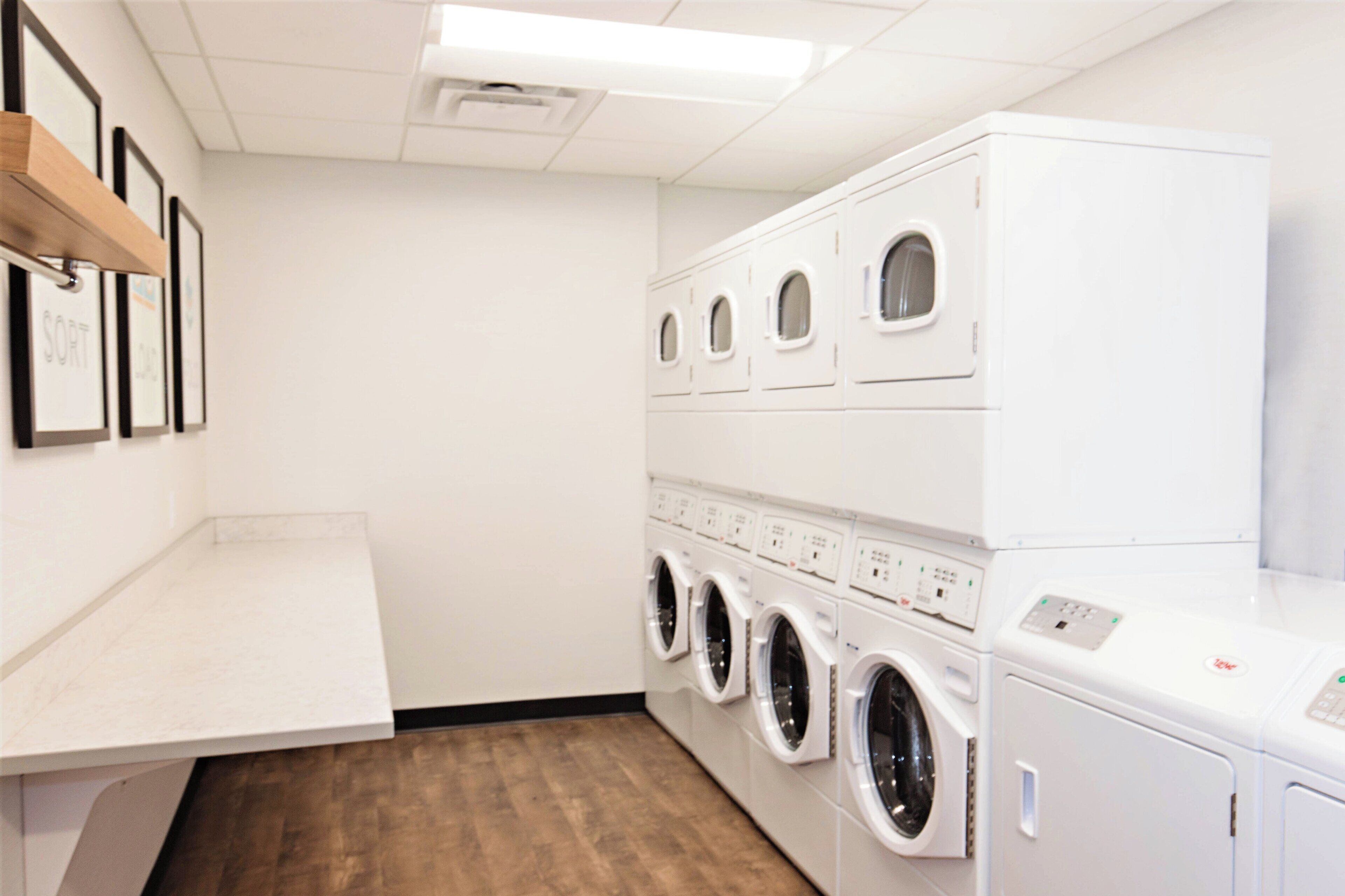 A laundry room with multiple washing machines and dryers, wooden shelves, and a tiled floor.