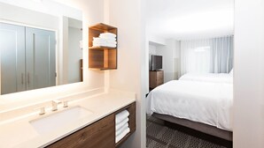 A hotel bathroom with a large mirror, a sink, and a shelf with towels. - Staybridge Suites Denver North - Thornton by IHG (Thornton)