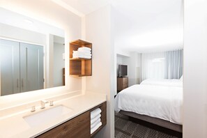 A hotel bathroom with a large mirror, a sink, and a shelf with towels. - Staybridge Suites Denver North - Thornton by IHG (Thornton)