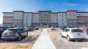A multi-story hotel with a central entrance, parking lot, and a clear sky. - Staybridge Suites Denver North - Thornton by IHG (Thornton)