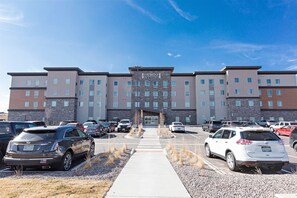 A multi-story hotel with a central entrance, parking lot, and a clear sky. - Staybridge Suites Denver North - Thornton by IHG (Thornton)