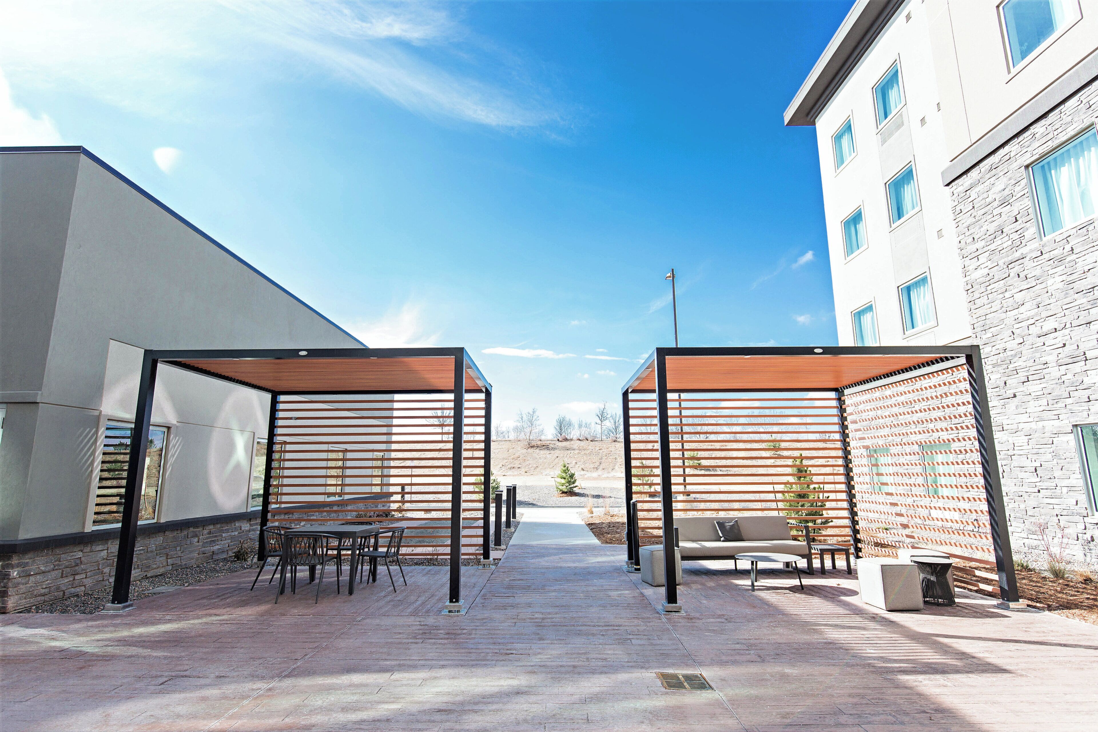 An outdoor patio area with wooden pergolas, seating, and a view of a building in the background.