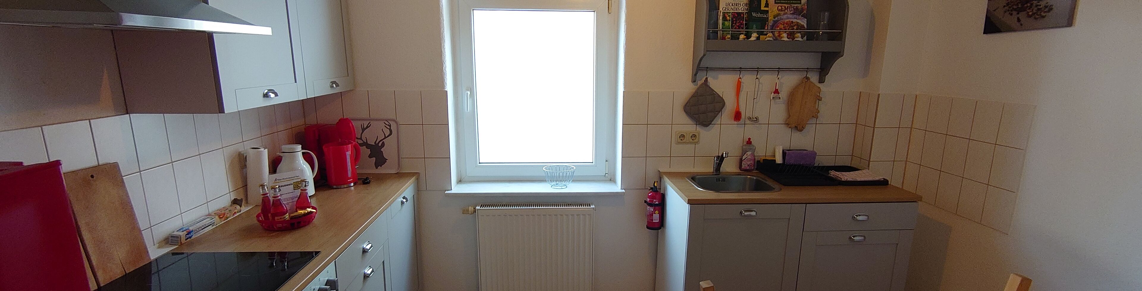 Eine kleine Küche mit Fenster, weißen Schränken, einer Spüle und einem Heizkörper.