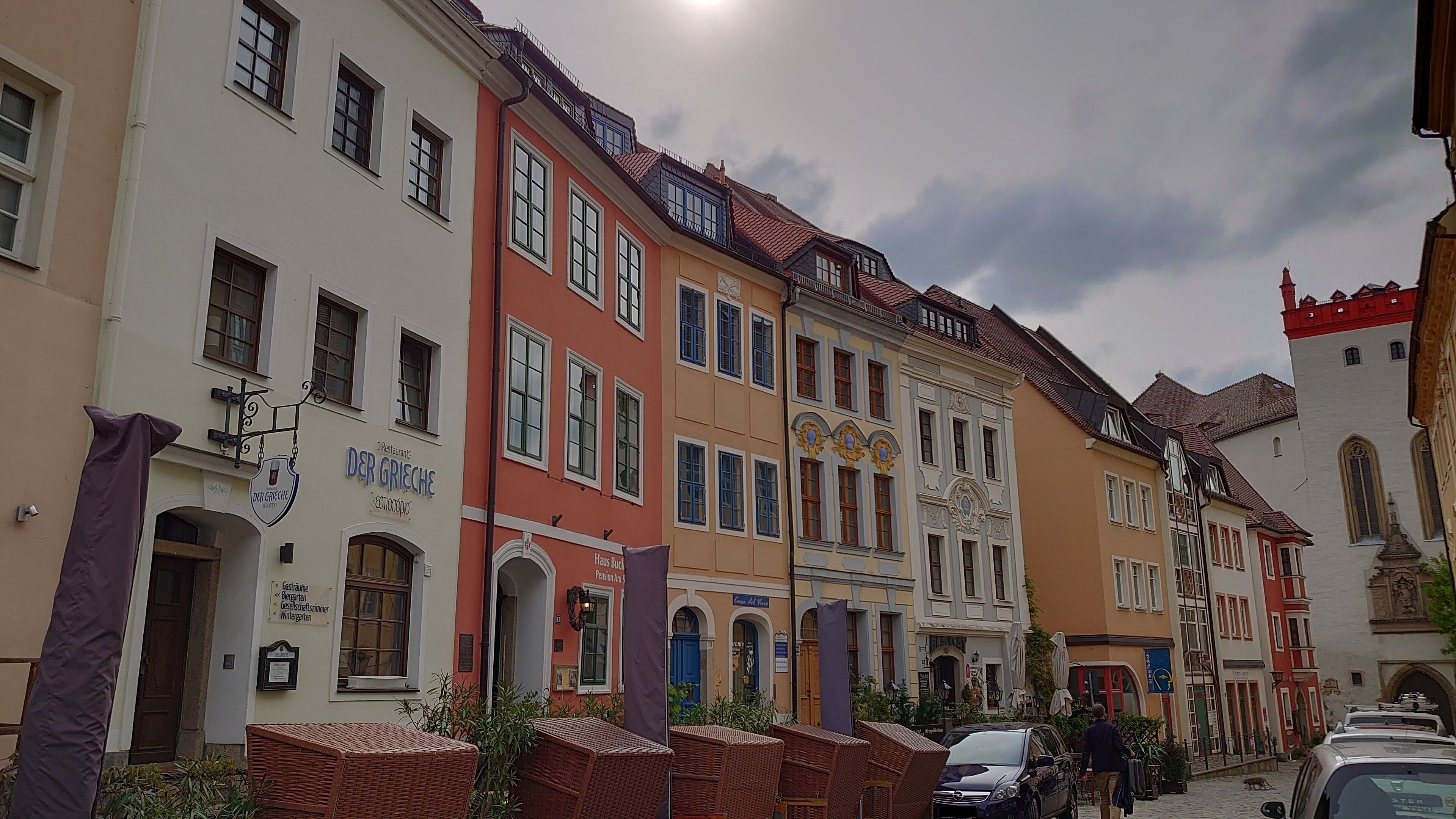 Een rij kleurrijke historische gebouwen, met een restaurant genaamd 'Der Griechische' aan de linkerkant.