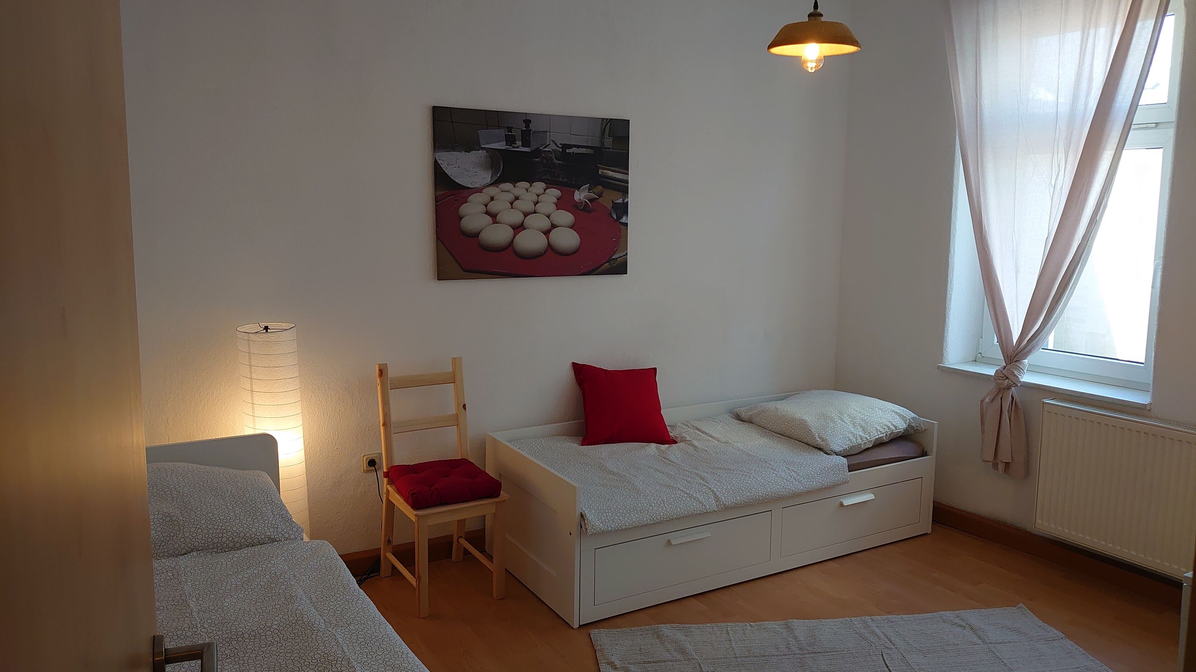 Une chambre à coucher avec un lit, une chaise, un radiateur et une fenêtre avec des rideaux.