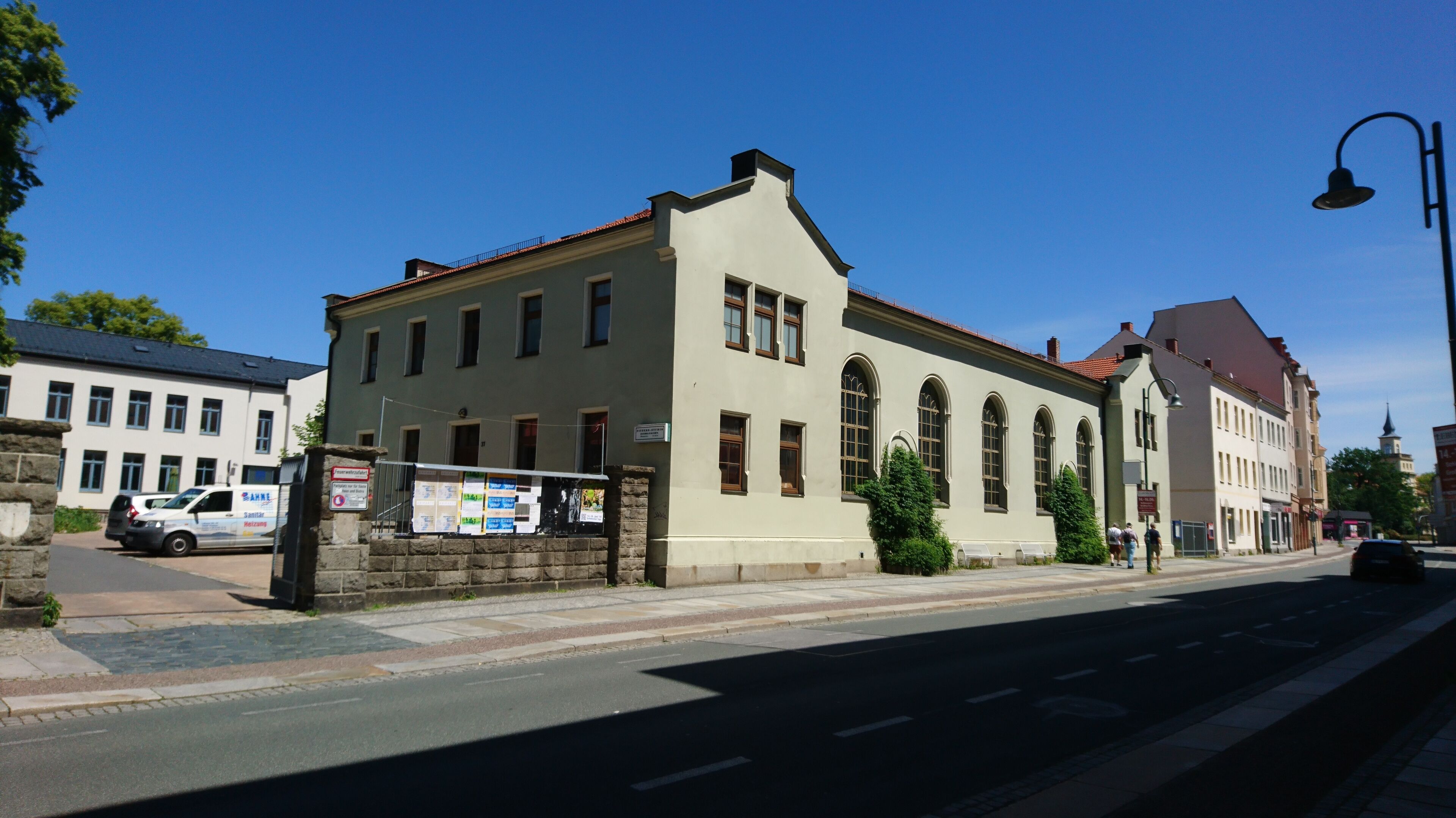 En byggnad med en ljus fasad, många fönster och ett rött tak. Det finns en skylt på byggnadens fasad och en parkerad skåpbil framför.