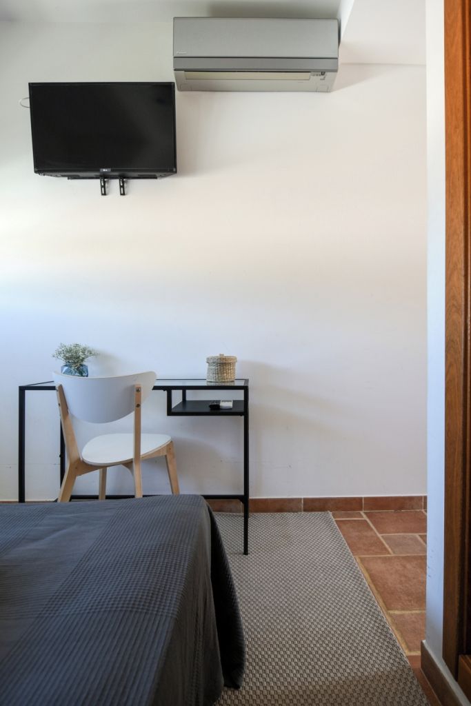 A bedroom with a bed, a desk, a chair, a television, and an air conditioning unit.