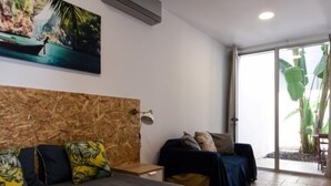 A modern hotel room with a large bed, a wooden headboard, a painting of a tropical scene, and a sliding glass door leading to a balcony with plants. - Pé na Areia (Castro Marim)