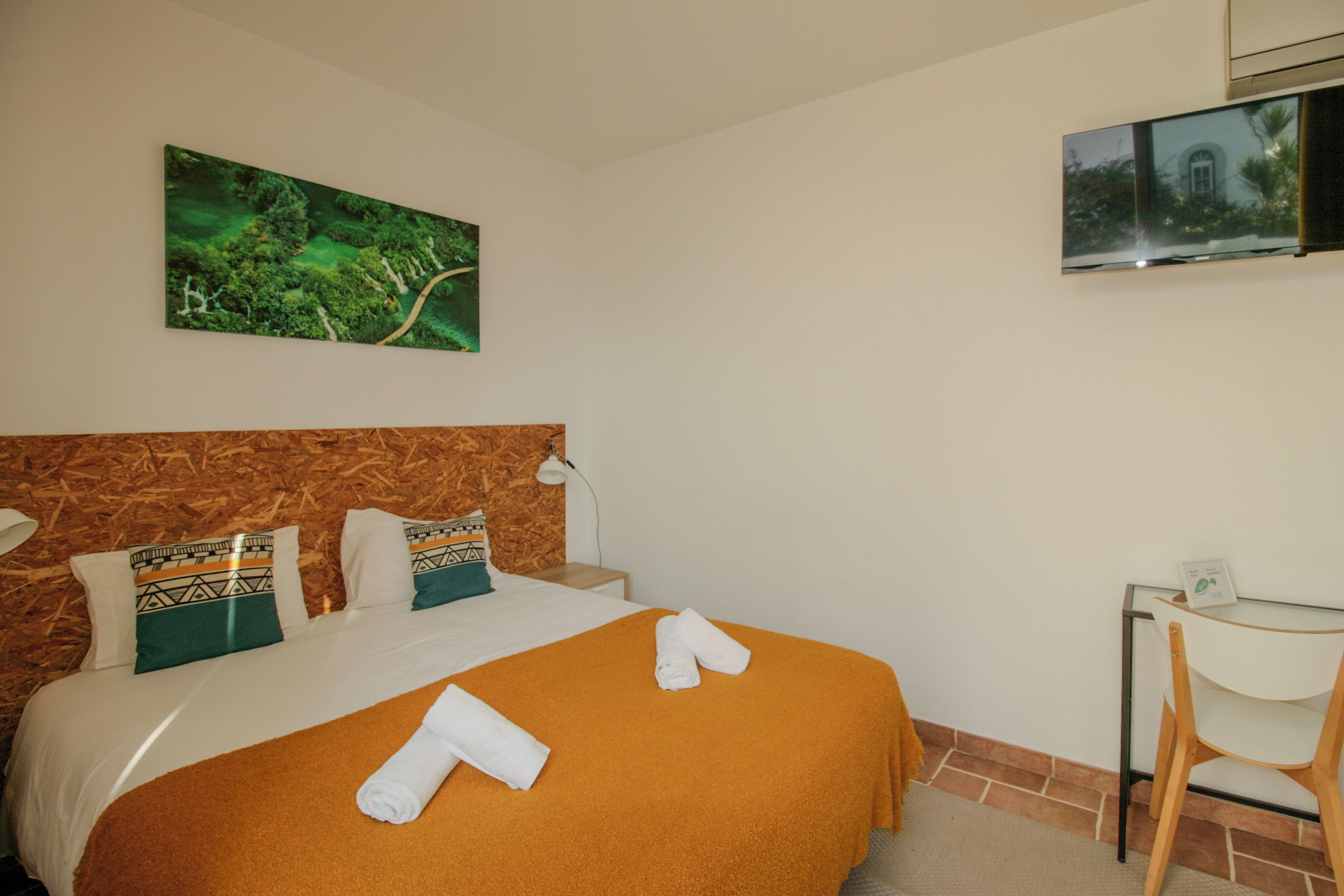 Habitación de hotel con cama, escritorio, televisor y un cuadro de un bosque.