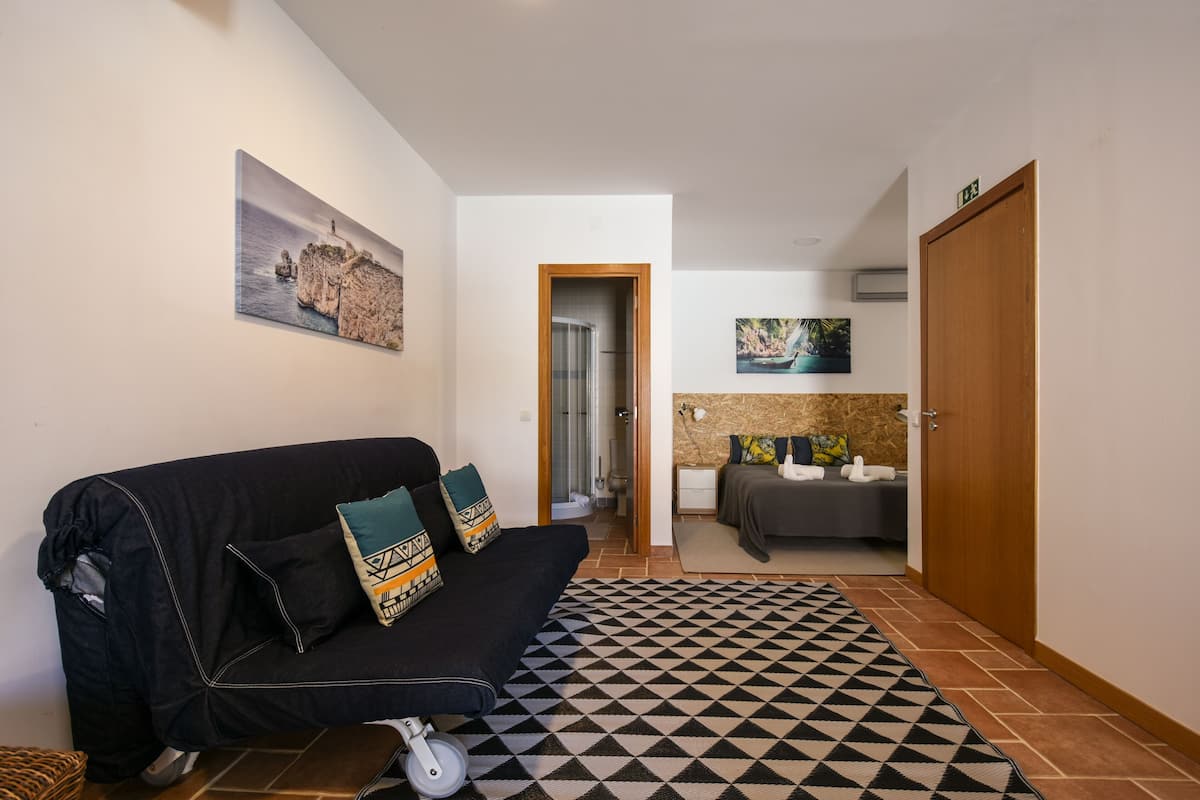A modern living room with a black sofa, patterned rug, and a painting of a coastal scene.