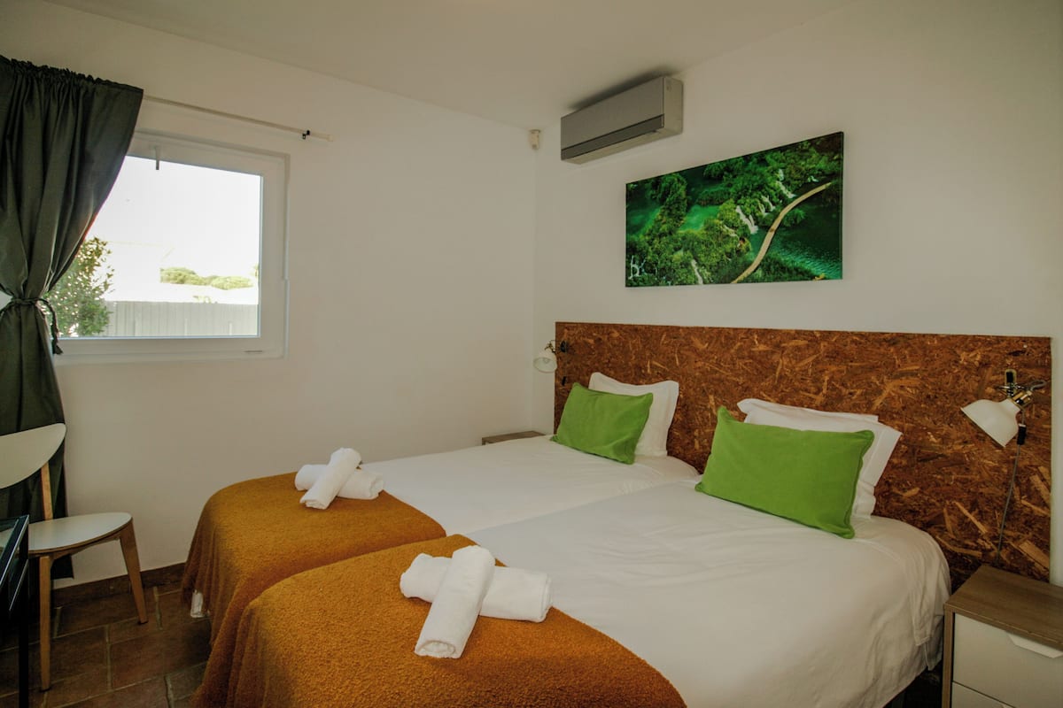 A hotel room with two beds, a window with curtains, a painting on the wall, and a wooden headboard.