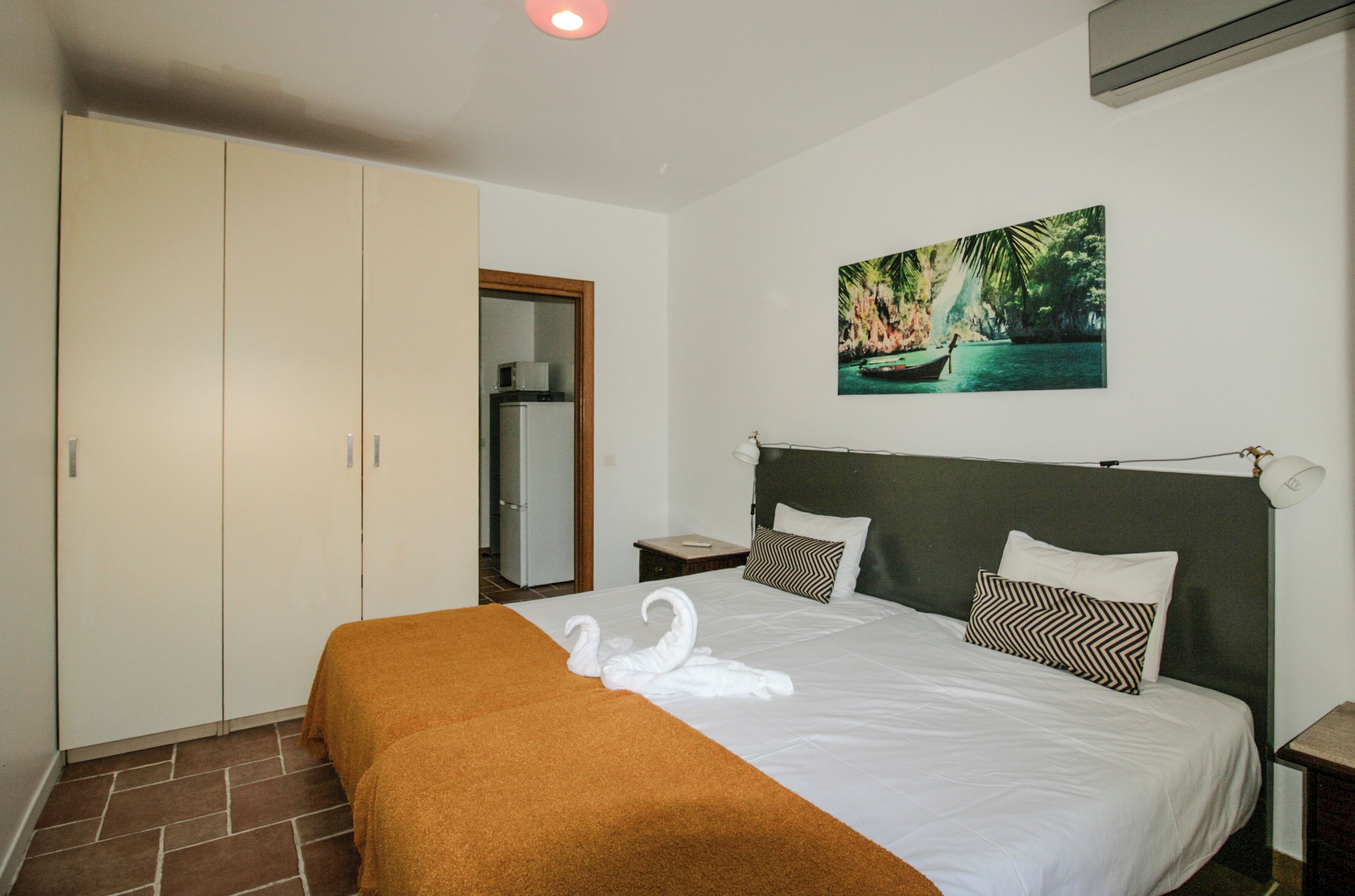A hotel room with a bed, a wardrobe, a nightstand, a painting, and a door.