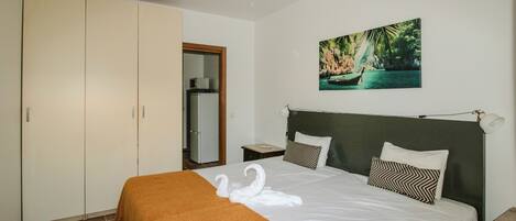 A hotel room with a bed, a wardrobe, a nightstand, a painting, and a door.