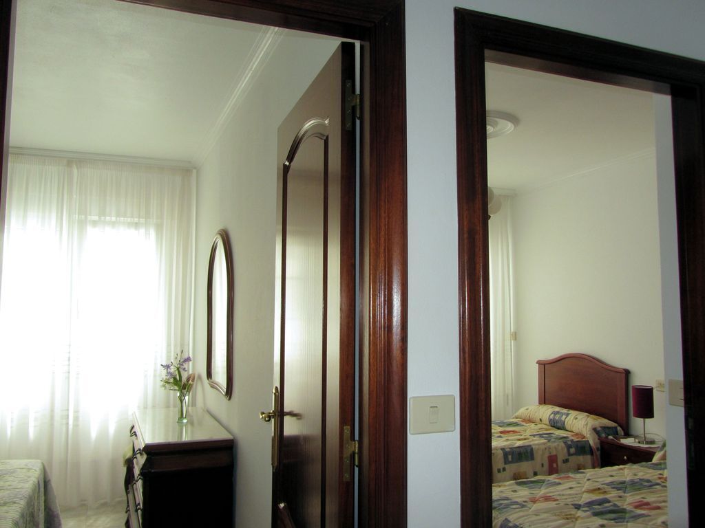 A hotel room with a bed, a bedside table, a mirror, and a window with curtains.