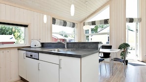 A modern kitchen with a central island, white cabinetry, and a large window providing natural light. - Holiday Home in Großenbrode (Grossenbrode)