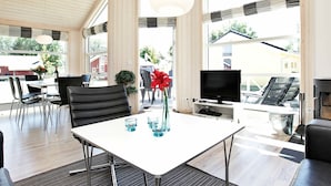 A modern living room with a white table, black chairs, a TV, and a fireplace. - Holiday Home in Großenbrode (Grossenbrode)