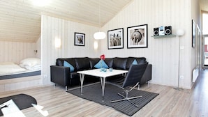 A modern room with a black leather sofa, a white table, and a black rug. There are framed pictures on the wall and a speaker on the right. - Holiday Home in Großenbrode (Grossenbrode)