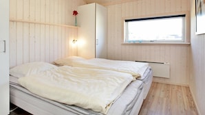 A bedroom with two beds, a window, a white wardrobe, and a wooden ceiling. - Holiday Home in Großenbrode (Grossenbrode)