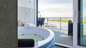 Et moderne badeværelse med et fristående badekar, en glas brusekabine og udsigt til en lysthavn med både og en strand.