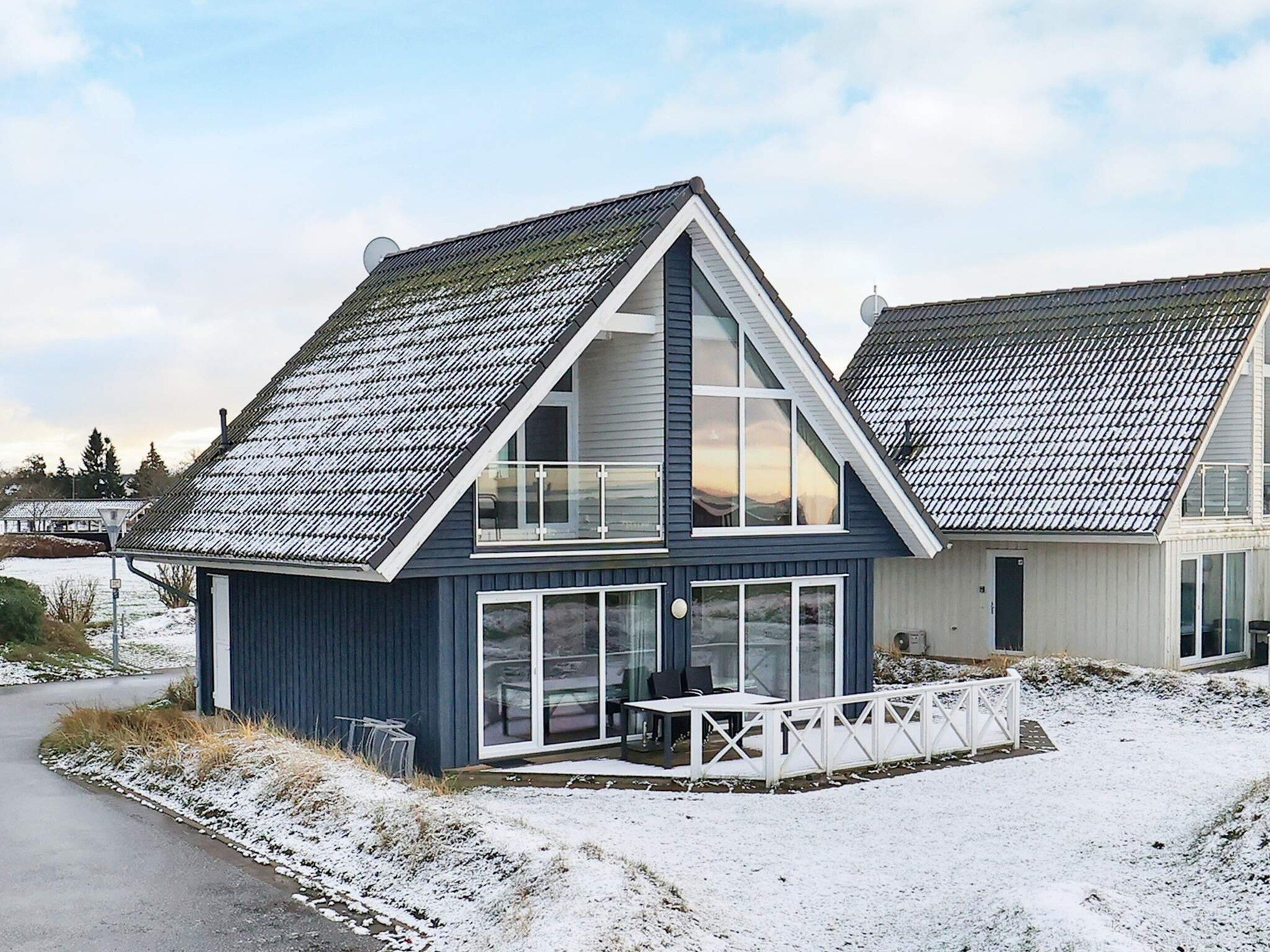 A two-story house with a sloped roof, large windows, and a covered outdoor seating area.