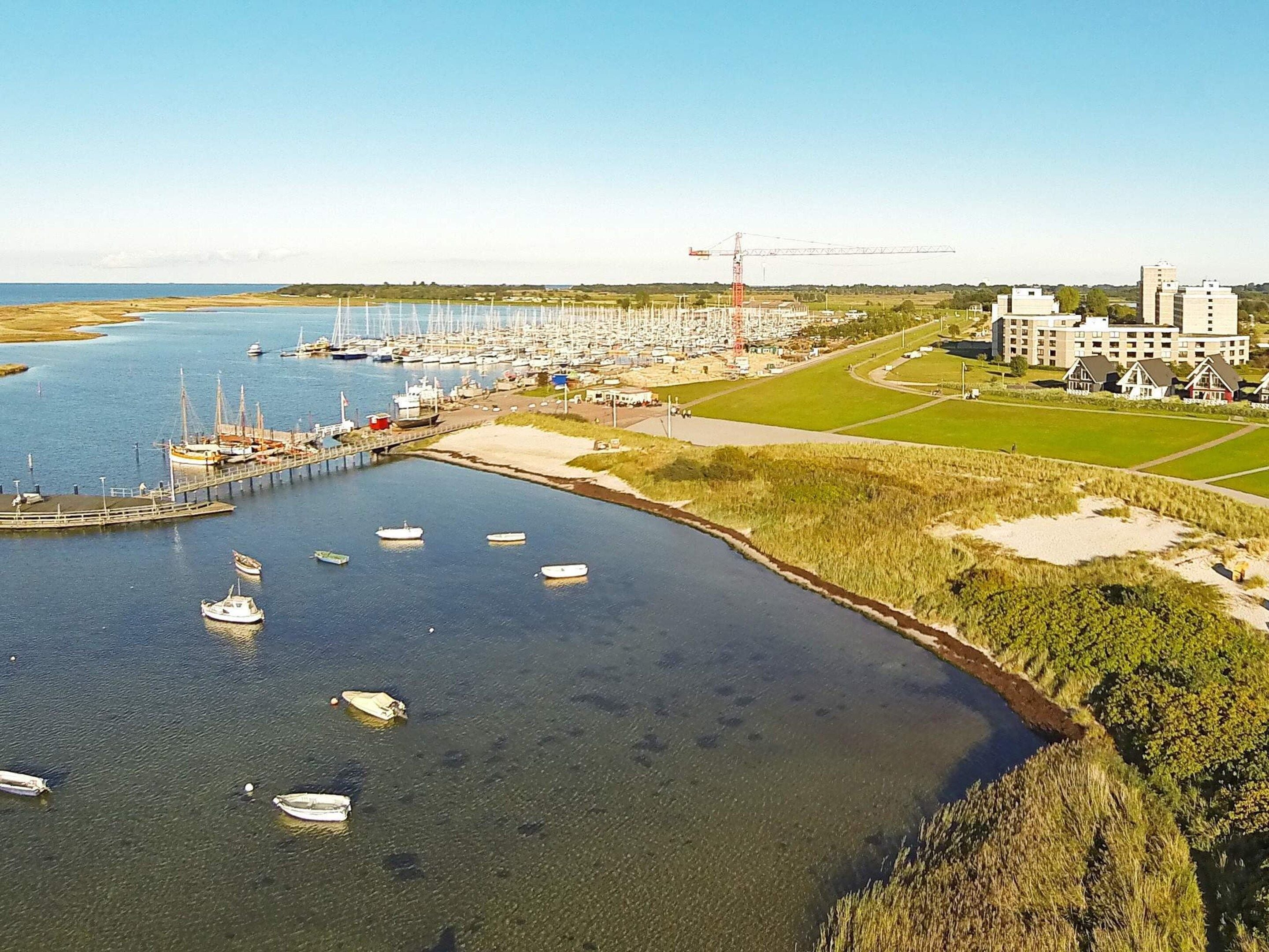 A marina with boats docked, a construction crane, and a building complex in the background.