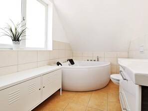 A modern bathroom with a freestanding bathtub, a white vanity, and a potted plant by the window. - Holiday Home in Wendtorf (Wendtorf)