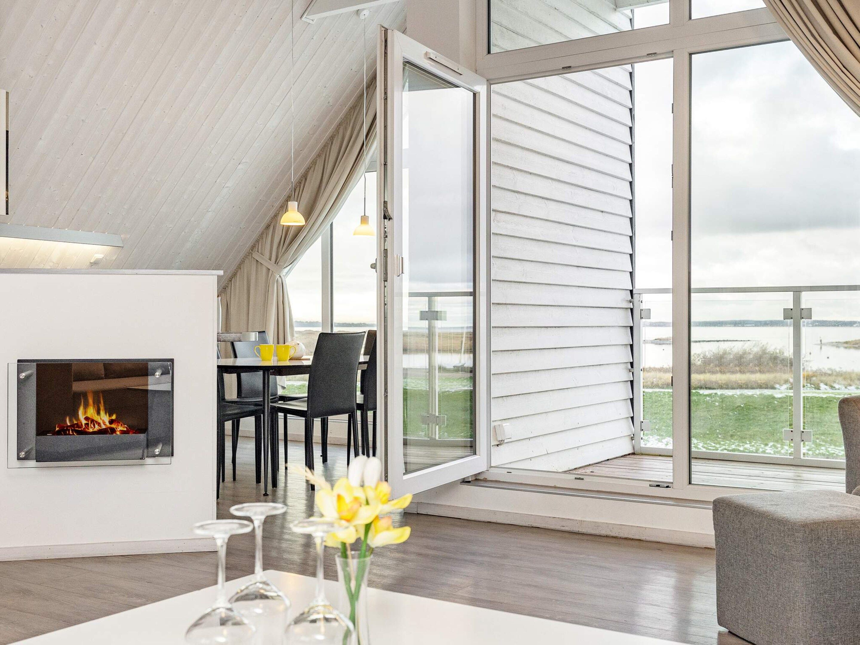 A modern interior with a fireplace, a dining area, and large windows offering a view of the outdoors.
