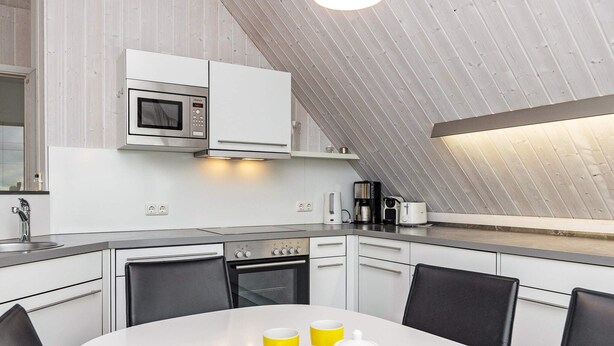 A modern kitchen with white cabinetry, a microwave, a stove, and a dining table with chairs.