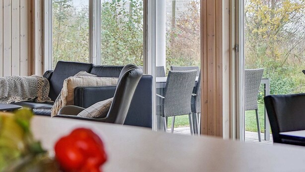 A modern interior with a sofa, dining table, and chairs, large windows with a view of greenery. - Holiday Home in Kappeln (Kappeln)