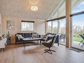 En modern inredning med ett träpanelat tak, ett stort fönster, en soffa, ett soffbord och en stol.