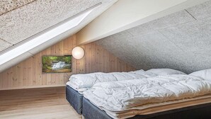A bedroom with a sloped ceiling, wooden walls, a bed with white bedding, a mounted TV, and a round wall light. - Holiday Home in Kappeln (Kappeln)