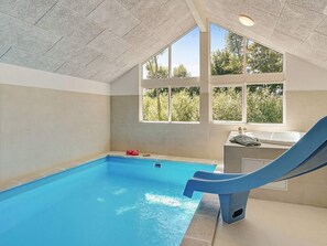An indoor swimming pool with a slide, large windows, and a view of trees. - Holiday Home in Kappeln (Kappeln)