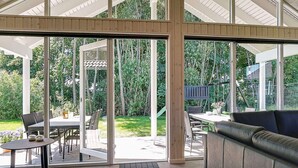 A covered patio with a table and chairs, a sofa, and a sliding glass door leading to a garden. - Holiday Home in Kappeln (Kappeln)