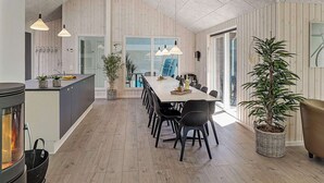 A modern kitchen with a central island, dining area with a long table and chairs, and a large window providing natural light. - Holiday Home in Kappeln (Kappeln)