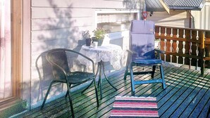 Une terrasse en bois avec une table et des chaises, une petite table recouverte d’une nappe en dentelle et une plante en pot.