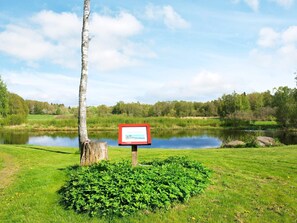 Un cadre paisible au bord d’un lac, avec un panneau indicateur, une végétation luxuriante et un ciel dégagé.