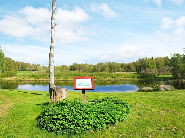 A serene lakeside setting with a signboard, lush greenery, and a clear sky.