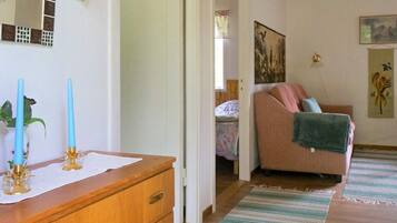 A room with a wooden dresser, a bed with a floral bedspread, a pink sofa with a green towel, and a painting on the wall.