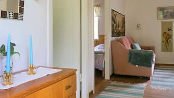 A room with a wooden dresser, a bed with a floral bedspread, a pink sofa with a green blanket, and a painting on the wall.