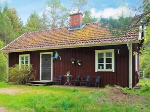 Ett litet, envåningshus byggt av trä med ett tak täckt av takpannor, en ytterdörr och en liten veranda med fyra stolar.