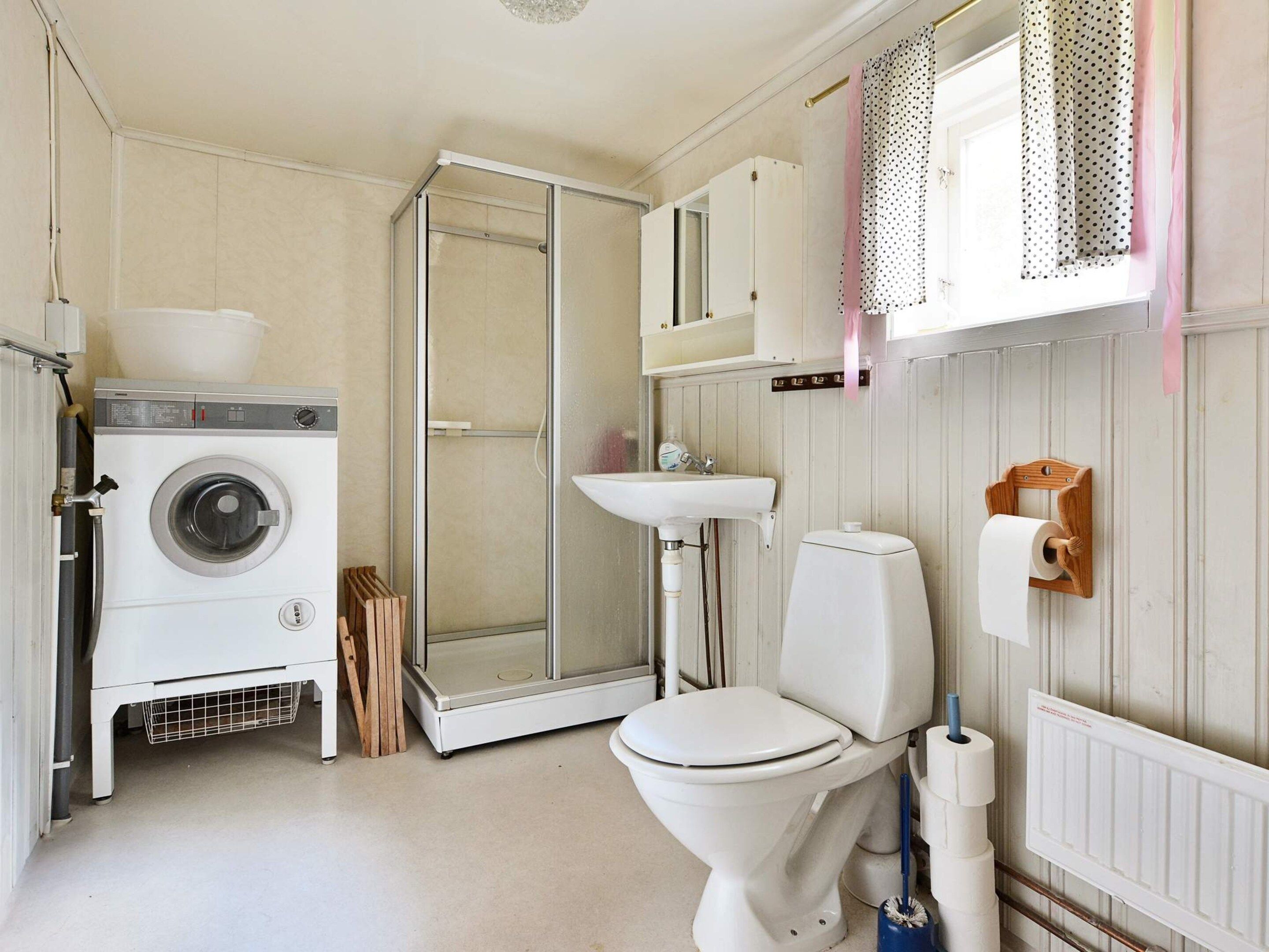 A compact bathroom with a washing machine, toilet, shower, and sink.