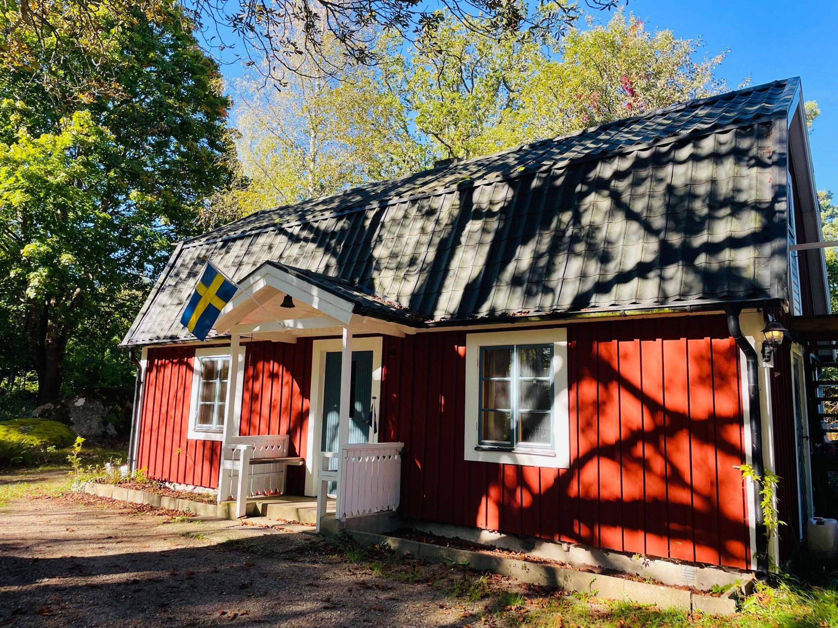 A red wooden cabin with a porch, a flag, and a window.