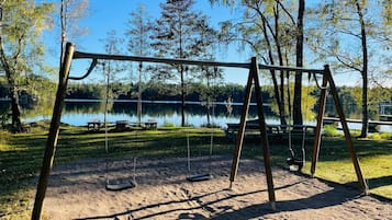 Columpios en un parque con mesas de picnic y un lago al fondo.