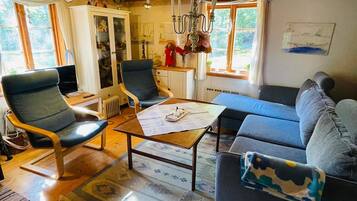 Una sala de estar acogedora con techo de madera, un sofá, dos sillones, una mesa de centro y una televisión.