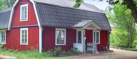 A red wooden house with a porch and a metal roof.