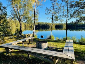 Uma área de piquenique à beira do lago, com bancos e uma lareira.