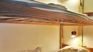 Una cama litera con cabecera de madera, una lámpara de noche y un almohadón a rayas.