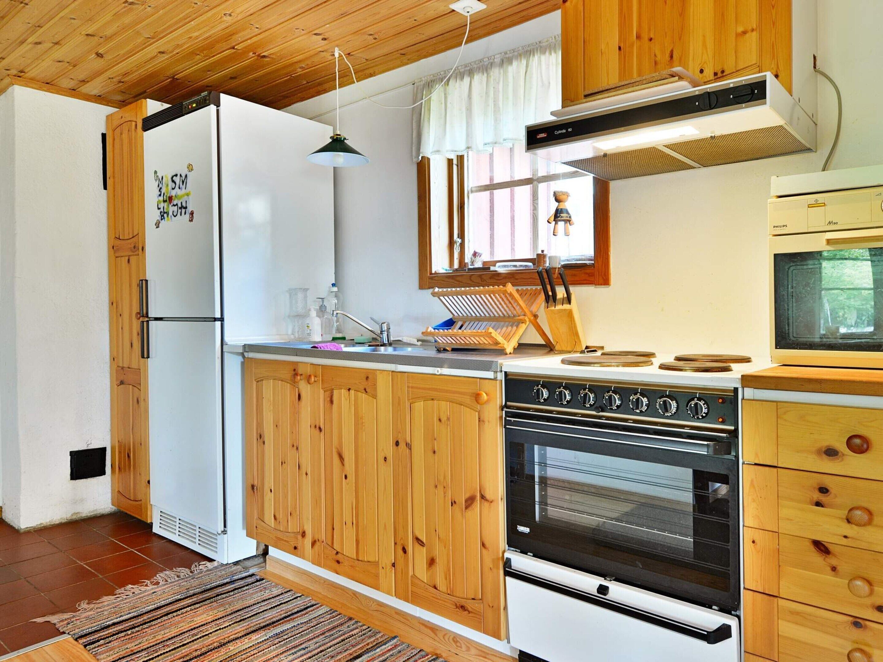 Cocina compacta con armarios de madera, horno empotrado, microondas y techo de madera.